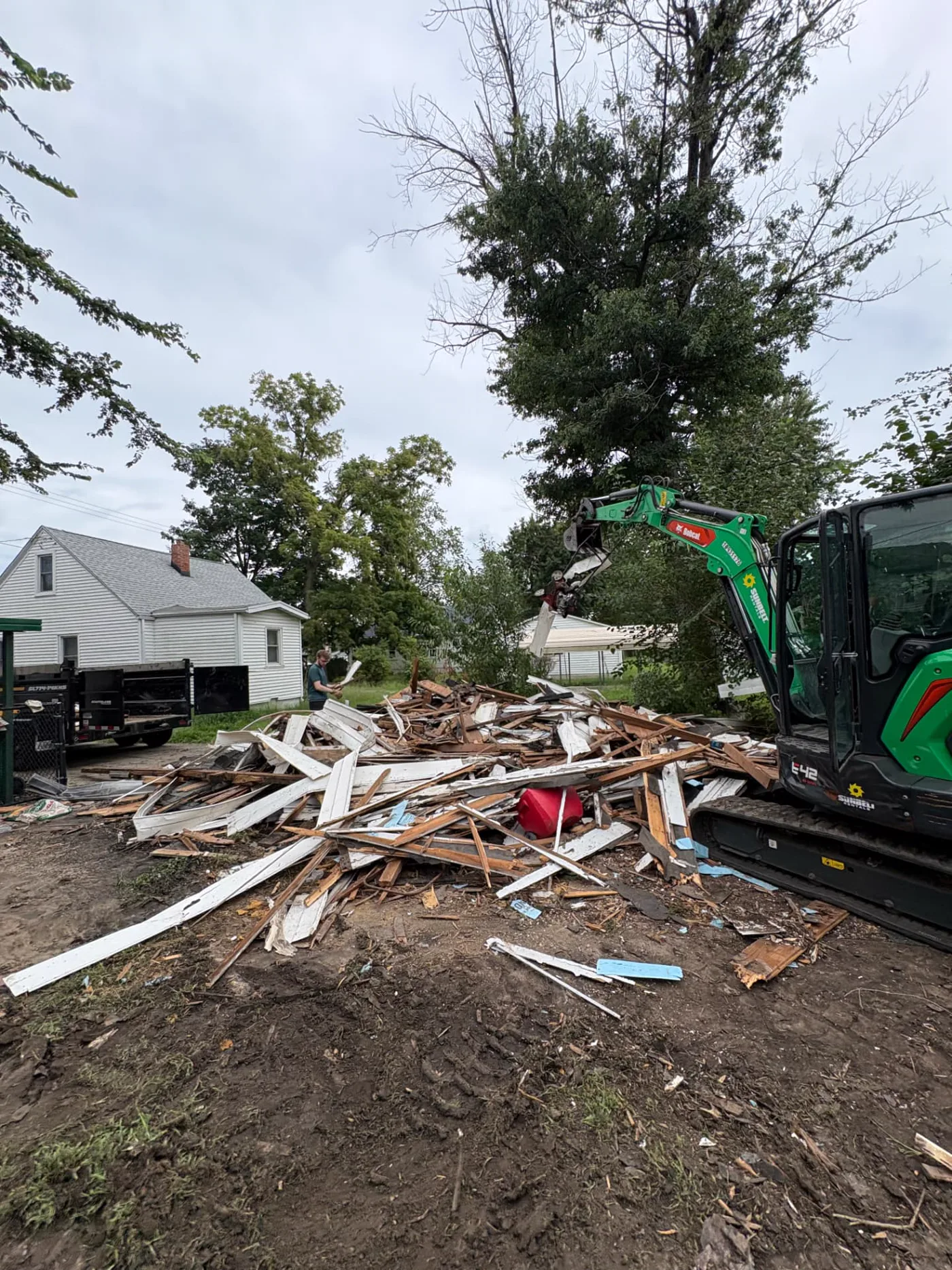 Compact excavator sorting lumber and siding during a garage demolition